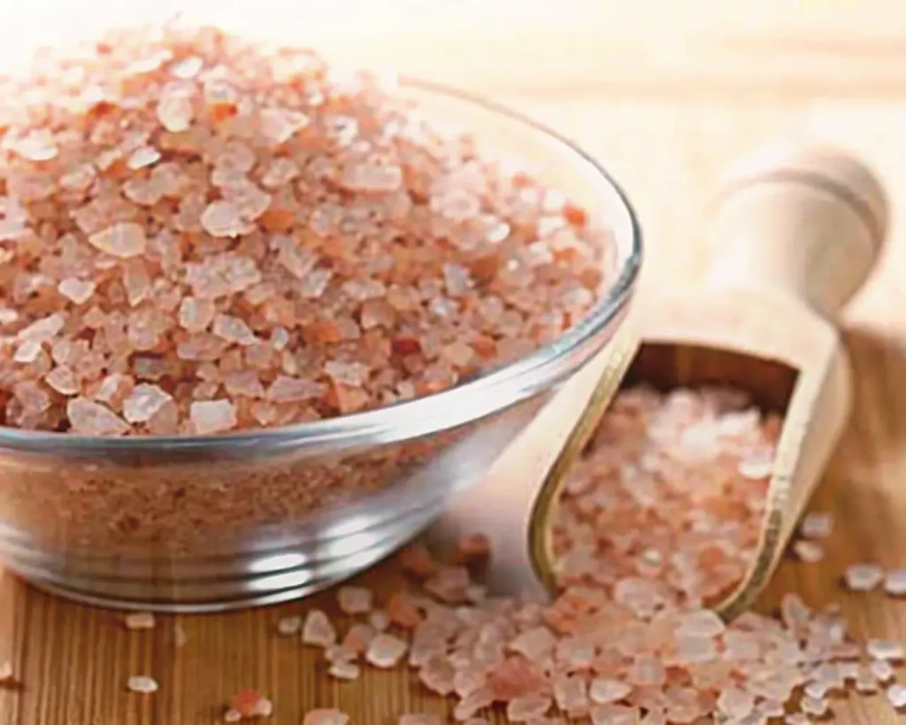 Himalayan pink salt in glass bowl with measuring wooden spoon