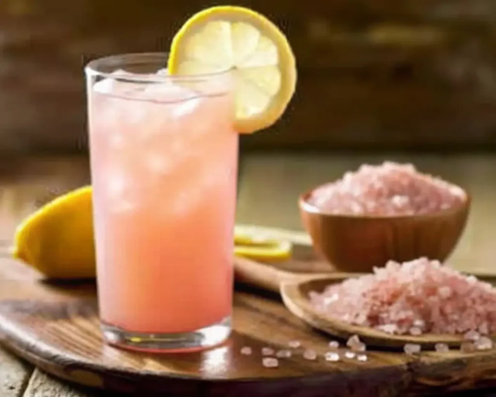 Refreshing Himalayan pink salt lemon drink for weight loss on rustic board with fresh lemon and pink salt crystals displayed.