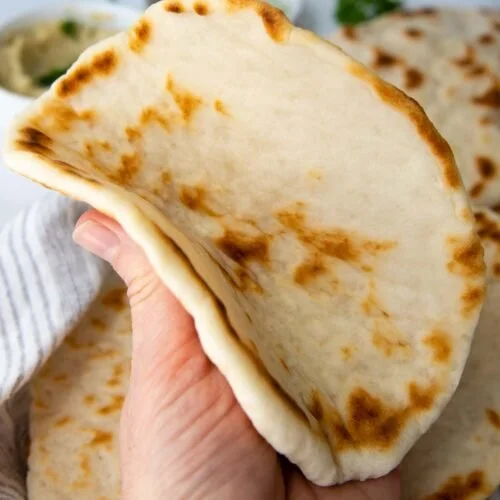 Homemade gluten-free flat bread on a wooden board with fresh herbs.